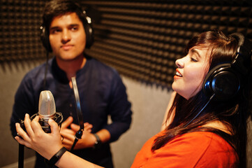 Young asian duet singers with microphone recording song in record music studio.