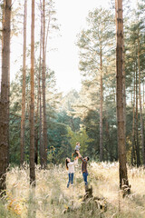 Outdoor portrait of happy young parents, having fun and lifting up their little cute baby son, during walk in autumn forest at sunny day