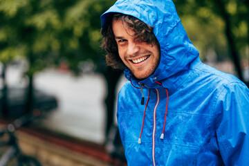 Closeup portrait of a happy man smiling, wearing blue raincoat during the rain outside. Cheerful...