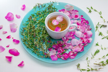 Homemade herbal tea in a white cup. Tea rose petals and thyme on a plate -ingredients for hot healthy drink