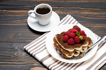 portion of Classic tiramisu dessert with raspberries and cup of espresso coffee isolated on wooden background