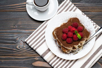 portion of Classic tiramisu dessert with raspberries and cup of espresso coffee isolated on wooden background