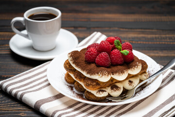portion of Classic tiramisu dessert with raspberries and cup of espresso coffee isolated on wooden background