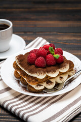portion of Classic tiramisu dessert with raspberries and cup of espresso coffee isolated on wooden background