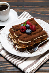 portion of Classic tiramisu dessert with raspberries. blueberries and cup of espresso coffee isolated on wooden background