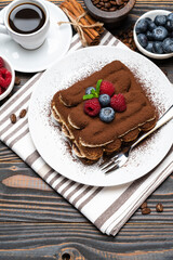 portion of Classic tiramisu dessert with raspberries. blueberries and cup of espresso coffee isolated on wooden background