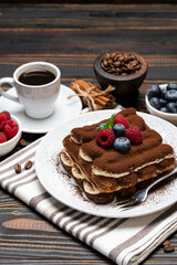 portion of Classic tiramisu dessert with raspberries. blueberries and cup of espresso coffee isolated on wooden background