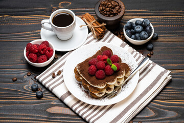 portion of Classic tiramisu dessert with raspberries. blueberries and cup of espresso coffee isolated on wooden background