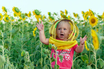 A joyful little girl dressed in a beekeeper's mask waves her hands against the background of a field with sunflowers. Beekeeping concept