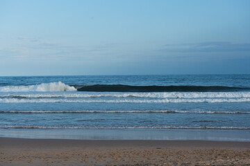 Sunset at the beach with clouds spread in the sky and calm waves of water of the ocean in the background