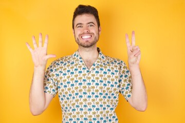 Young caucasian man with short hair wearing red shirt standing over isolated yellow background showing and pointing up with fingers number seven while smiling confident and happy.