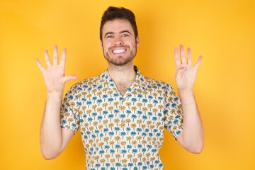 Young caucasian man with curly hair wearing red shirt standing over isolated yellow background showing and pointing up with fingers number nine while smiling confident and happy.
