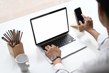 Croped shot of business woman using smartphone and laptop with white screen on work space.