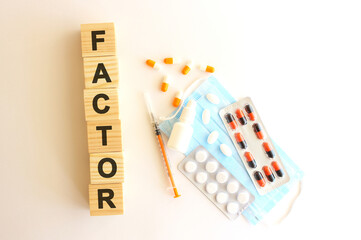 The word FACTOR is made of wooden cubes on a white background with medical drugs and medical mask. Medical concept.