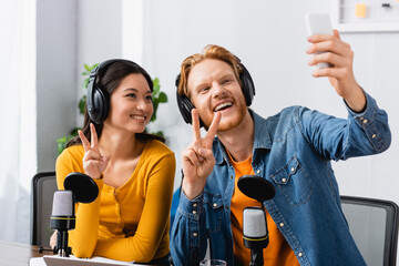 excited, redhead announcer taking selfie on mobile phone while showing victory signs together with...