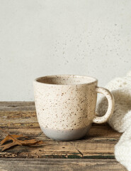 Two-tone mottled cup with a drink and a knitted blanket on an old wooden table