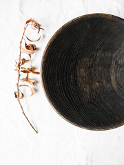 Wooden homemade big black bowl and dry branch with leaves on white cloth background. Top view. Copy space