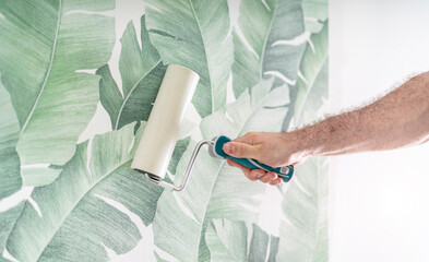 Tapezierer drückt die frisch verklebte Mustertapete mit der Rolle an die Wand 