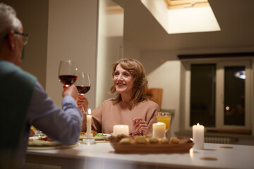 Senior couple sitting at the table and toasting with red wine during dinner in the kitchen