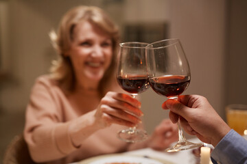Close-up of mature woman drinknig red wine with her friend during dinner at the table