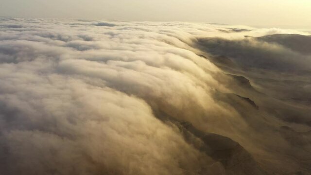 Nature amazing phenomenon of cloud surfing above mountains rock in desert. Magical moment above the clouds at sunrise. Shot from mountain peak highrise skyline. Dreaming mystical scene