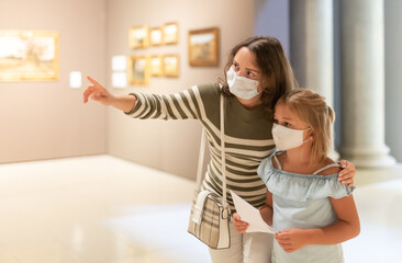 Mom and daughter in protective masks inspect the exhibits of the museum