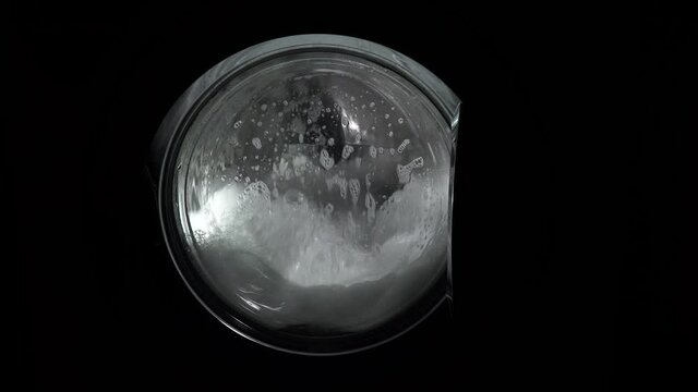 The problem is with an overdose or the wrong choice of detergent, a lot of foam. Close up. The washing machine on a black, dark background. Spinning drum. The washing process in the washing machine.