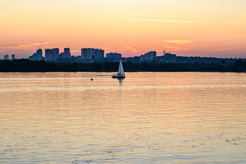 Sailing boat against the sunset behind modern buildings.