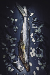 Still life, taken with the lightpainting technique, of a dried flying fish, with almonds and olive oil, on a rustic navy blue table. A typical meal from the Malaga and Cadiz area (Andalucia, Spain)