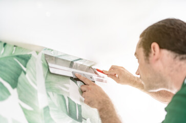 Tapezierer schneidet die Tapete an der Decke mit dem Messer ab