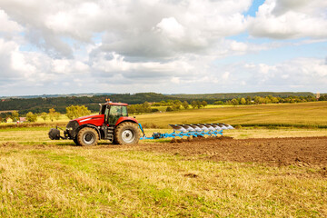 Farmer in a big red tractor preparing land with plow for sowing