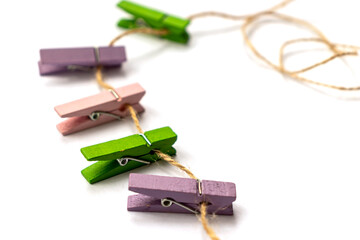 Multicolored wooden clothespins lies on a rope on white background