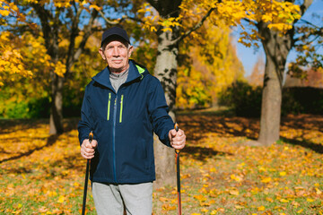 Smiling old man resting in autumn park after nordic walking. Senior athlete outdoors