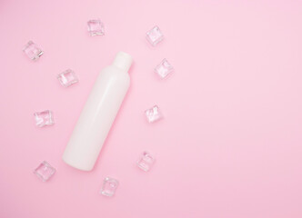 White plastic bottle for shampoo or other cosmetics. Ice cubes around, pink background, free space for text, top view.
