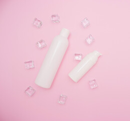 Body and skin care, cosmetology. White plastic bottle for shampoo and other cosmetics. Ice cubes around, pink background, free space for text, top view.