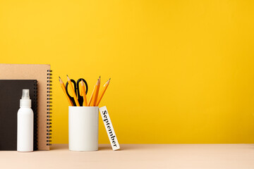 Cup of pencils and notepads on desk against yellow background