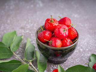 Ripe red cherries in a ceramic bowl with leaves on stone background