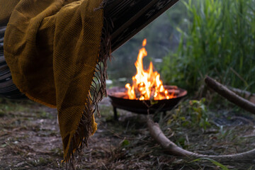 Mustard blanket on boho hammock next to lake and fire in firepit at dusk