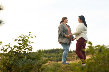 Overweight lesbians holding hands and dancing on the top of the hill outdoors