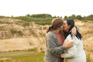 Young overweight lesbian couple embracing and kissing outdoors with beautiful view in the background