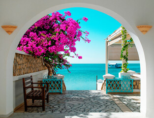 A view of the blue sea of ​​Tunisia through a white archway with pink blooming flowers in the...