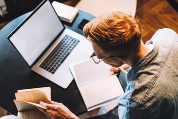 Focused caucasian man college student in glasses studying with books laptop distantly preparing for...