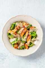 Caesar salad. Grilled chicken breast slices, green romaine salad leaves, croutons and parmesan, the classic recipe on a white marble background with a place for text