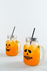Iced pumpkin cocktails in glass jars decorated with scary faces on the gray table, white background. Halloween Party mocktails. Vertical orientation, copy space