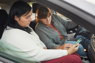 Two young overweight women driving car using navigator on mobile phone they looking direction on...
