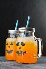 Iced pumpkin cocktails in glass jars decorated with scary faces on the chalkboard, black background. Halloween Party mocktails. Vertical orientation, copy space
