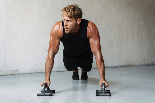 Photo of athletic young sportsman working out with push-up stops