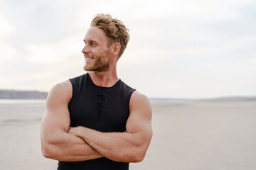 Photo of athletic happy sportsman smiling and posing on summer beach