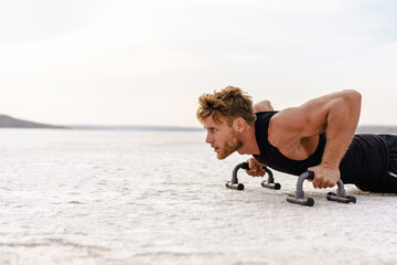 Photo of athletic young sportsman working out with push-up stops