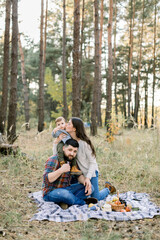 Happy family, handsome father, attractive mother and joyful little child toddler son, having fun together in autumn forest, sitting on blanket with fruits. Child is sitting on the shoulders of father